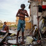 RIO DE JANEIRO, BRAZIL - MAY 22: A man bathes from a small hose amongst the remains of demolished homes in the Metro Mangueira favela, located near Maracana stadium, on May 22, 2014 in Rio de Janeiro, Brazil. The homes were thought to have been knocked down for a parking lot for the stadium, though that has yet to be built. The area has seen some people occupy certain dwellings. Evictions and demolitions have been occurring in Rio favelas ahead of the 2014 FIFA World Cup and Rio 2016 Olympic Games in spite of a housing shortage in the city. Rio's housing and urban planning goals include a planned five percent reduction of areas occupied by favelas by 2016. Alternative affordable housing, generally on the peripheries of the city, is unable to meet demand and some residents complain they have not received adequate compensation for demolished homes. (Photo by Mario Tama/Getty Images)